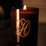 Glass candle in amber vessel with H emblem engraved and a lit flame