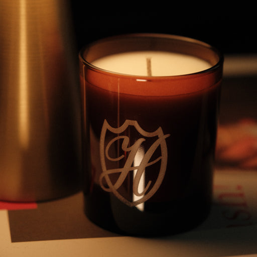 Unlit candle in brown glass vessel with gold etched H emblem in a shield