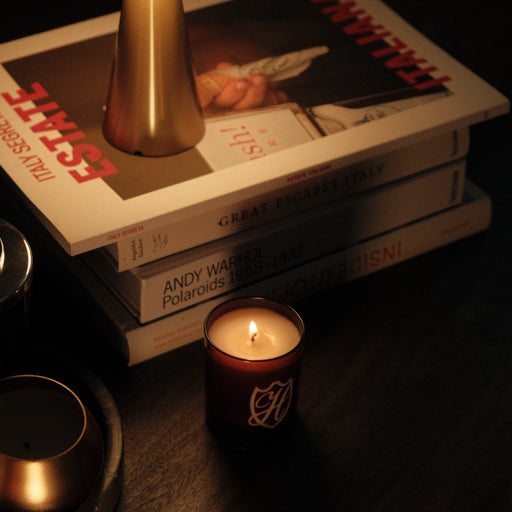 Coffee table with a stack of books, 70s style lamp & lit candle in an amber glass container.