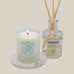 lit laundry room candle in vessel on marble slab with laundry room diffuser in bottle with reeds