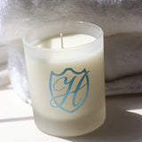 Glass soy wax candle with blue H emblem engraved on the holder