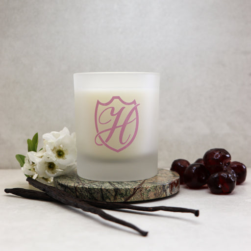 Glass candle with pink H logo sat on a stone coaster with flowers & herbs surrounding