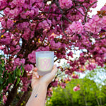 A candle being held in a hand in front of a vibrant pink cherry blossom tree